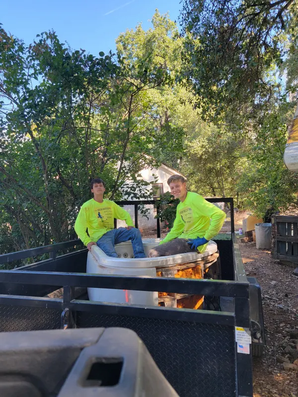 Two crew members in high-visibility shirts loading an old bathtub onto a trailer