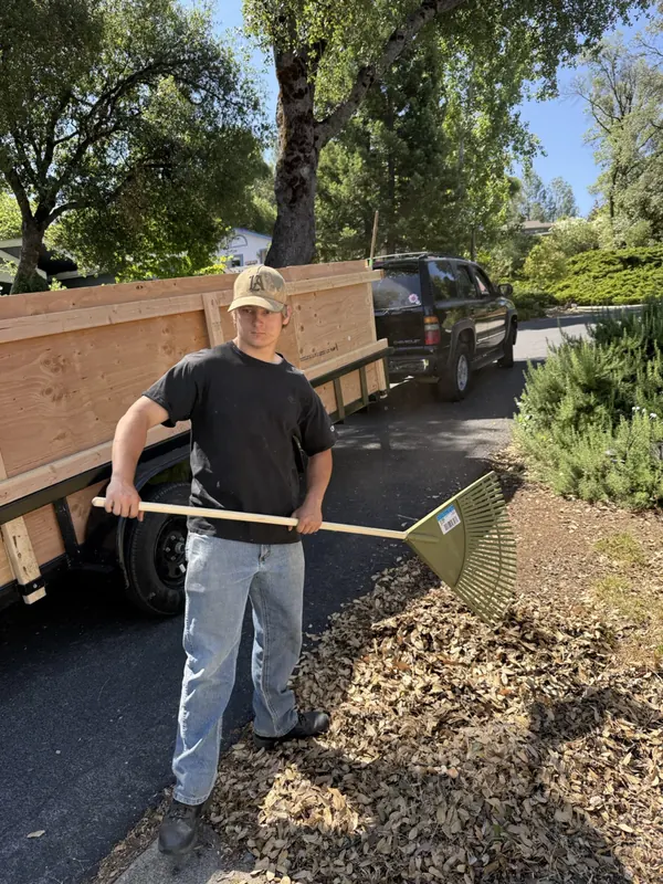 A crew member raking up the last of a debris pile beside a loaded trailer