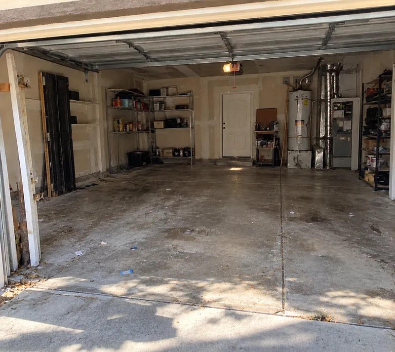 After: the same garage with a clear concrete floor and only the shelving and water heater left