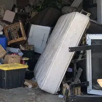 An old mattress leaning on a packed pile of boxes and furniture in a garage