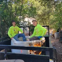 Two crew members in high-visibility shirts sitting in an old bathtub loaded on a trailer